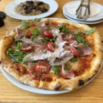 Pizza Prosciutto Crudo e Rucola z szynką parmeńską, rukolą i pomidorkami koktajlowymi podana na białym talerzu.