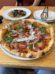 Pizza Prosciutto Crudo e Rucola z szynką parmeńską, rukolą i pomidorkami koktajlowymi podana na białym talerzu.