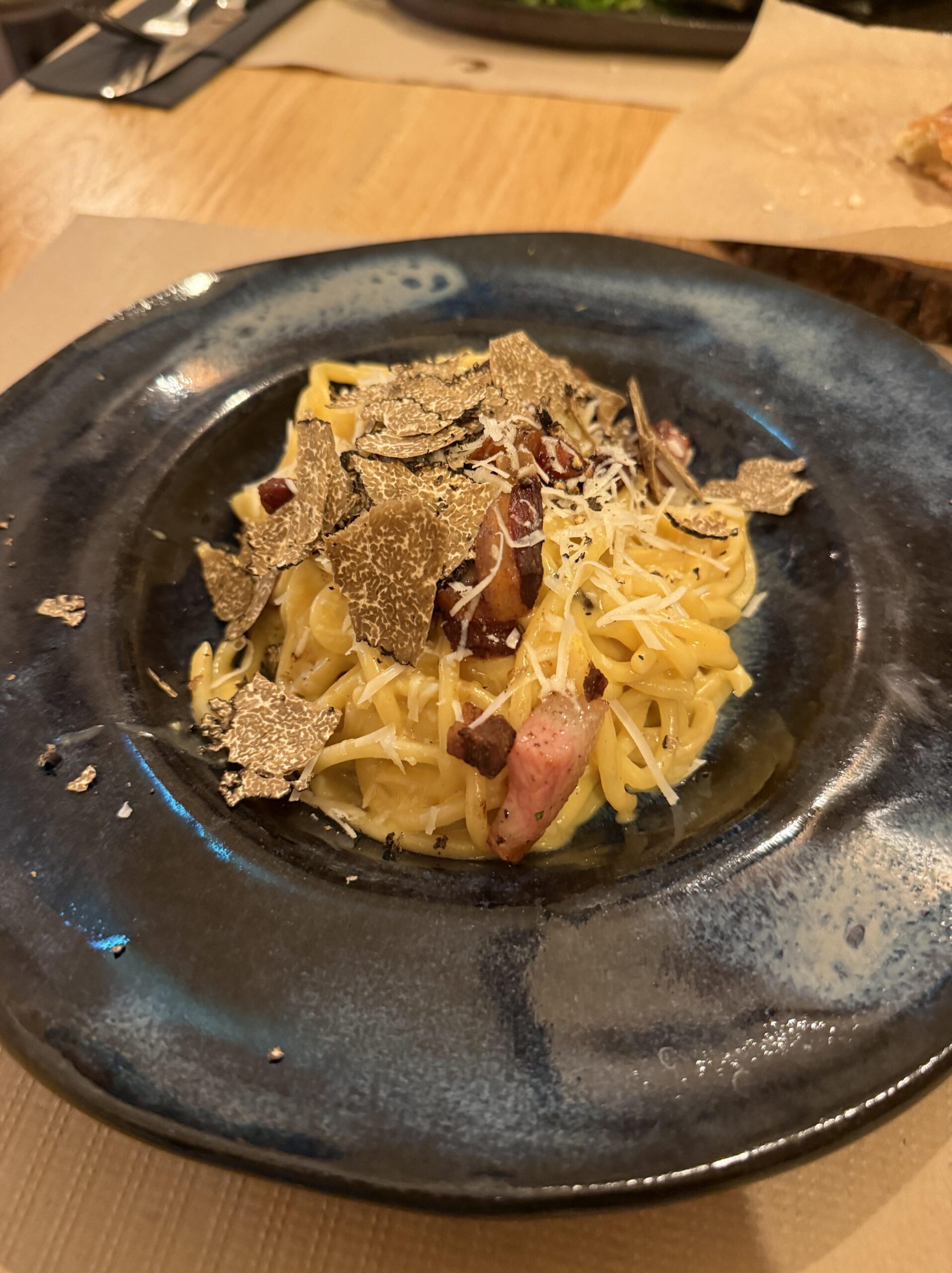 Makaron carbonara z chrupiącym guanciale, i plastrami trufli na ciemnym szkliwionym talerzu.